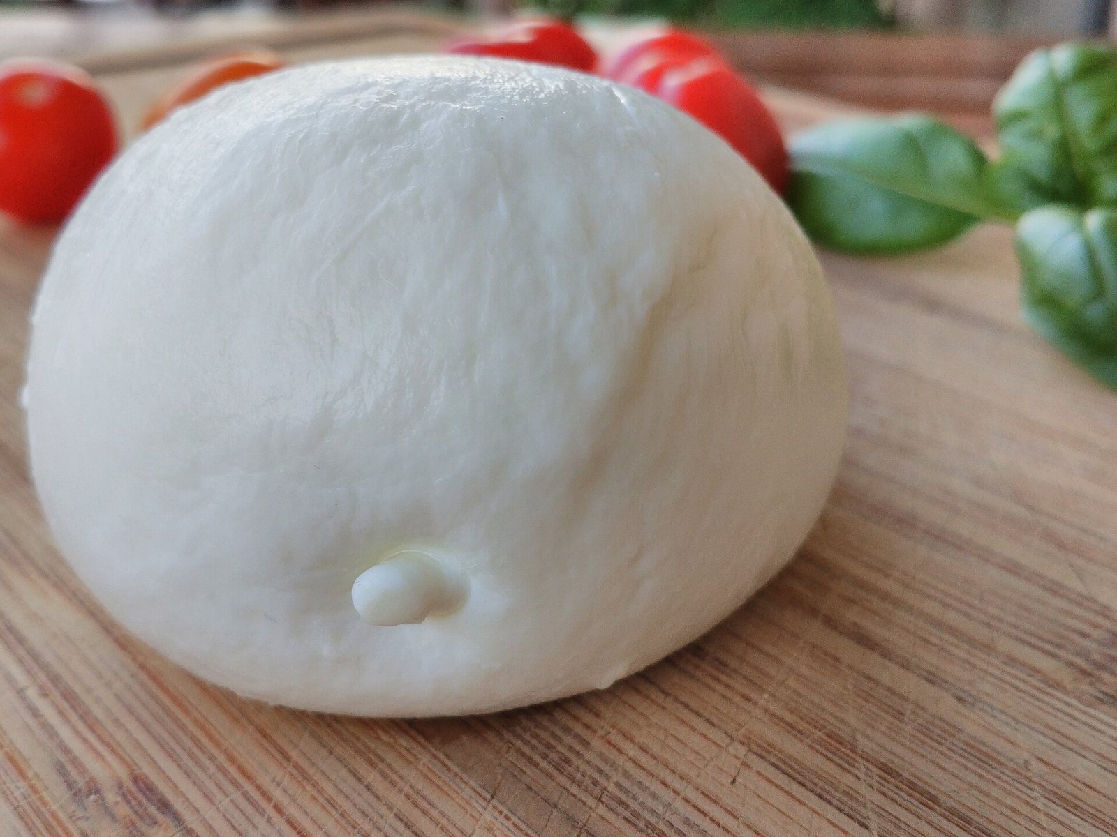 Mozzarella di bufala su tagliere di legno con pomodorini e foglie di basilico
